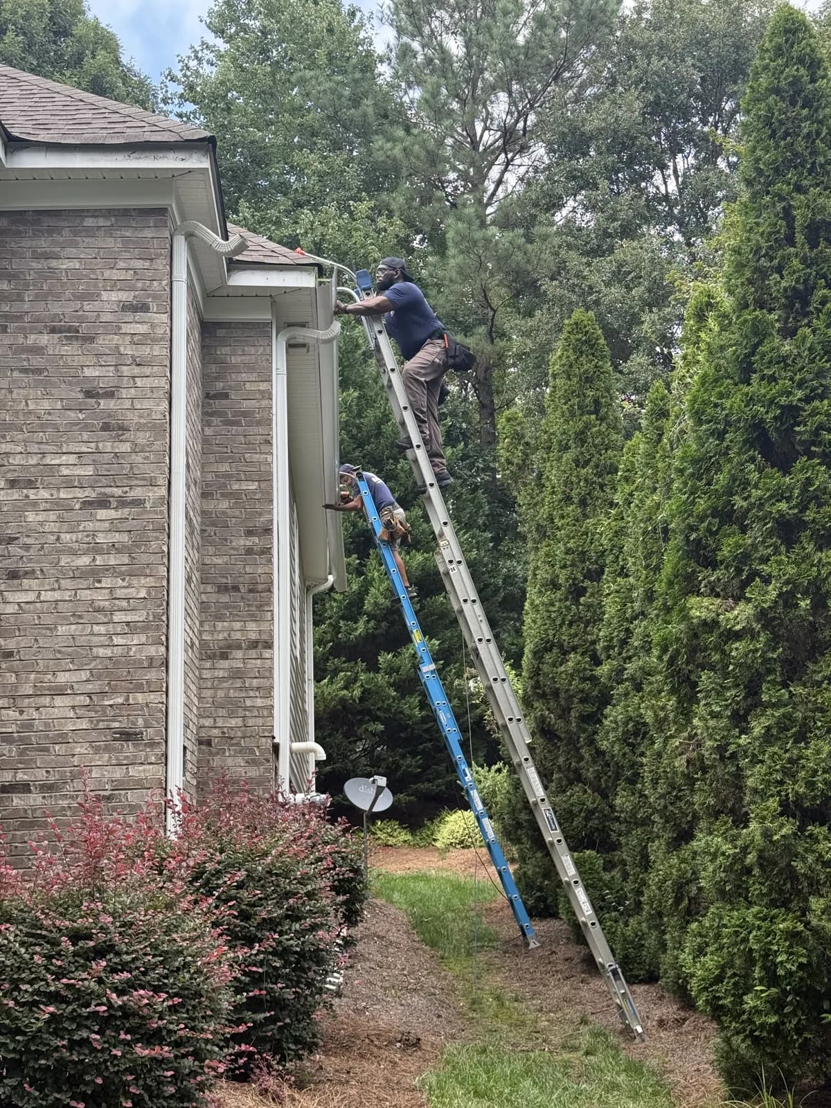Two Badger Gutters installers on ladders hanging a new gutter on a brick two-story in the Charlotte, NC area