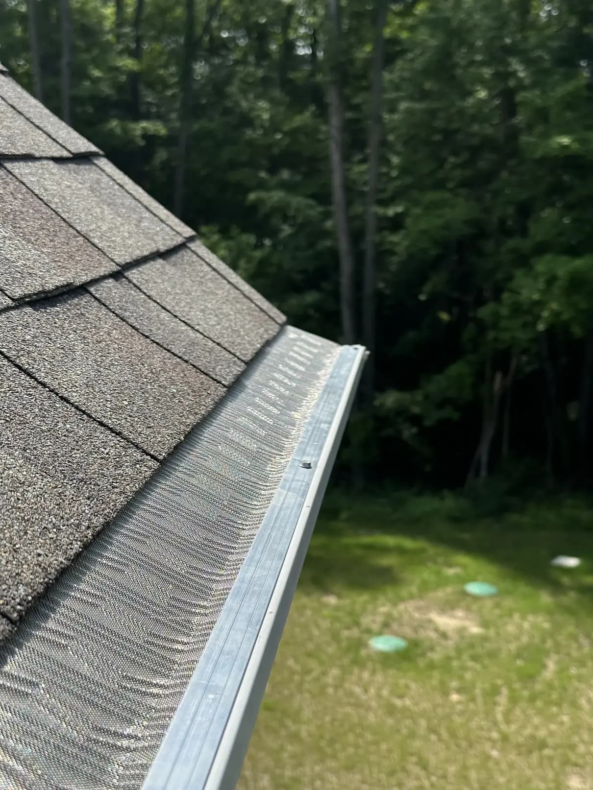 Stainless micro-mesh gutter guard on a gray gutter, looking down the run of a shingle roof