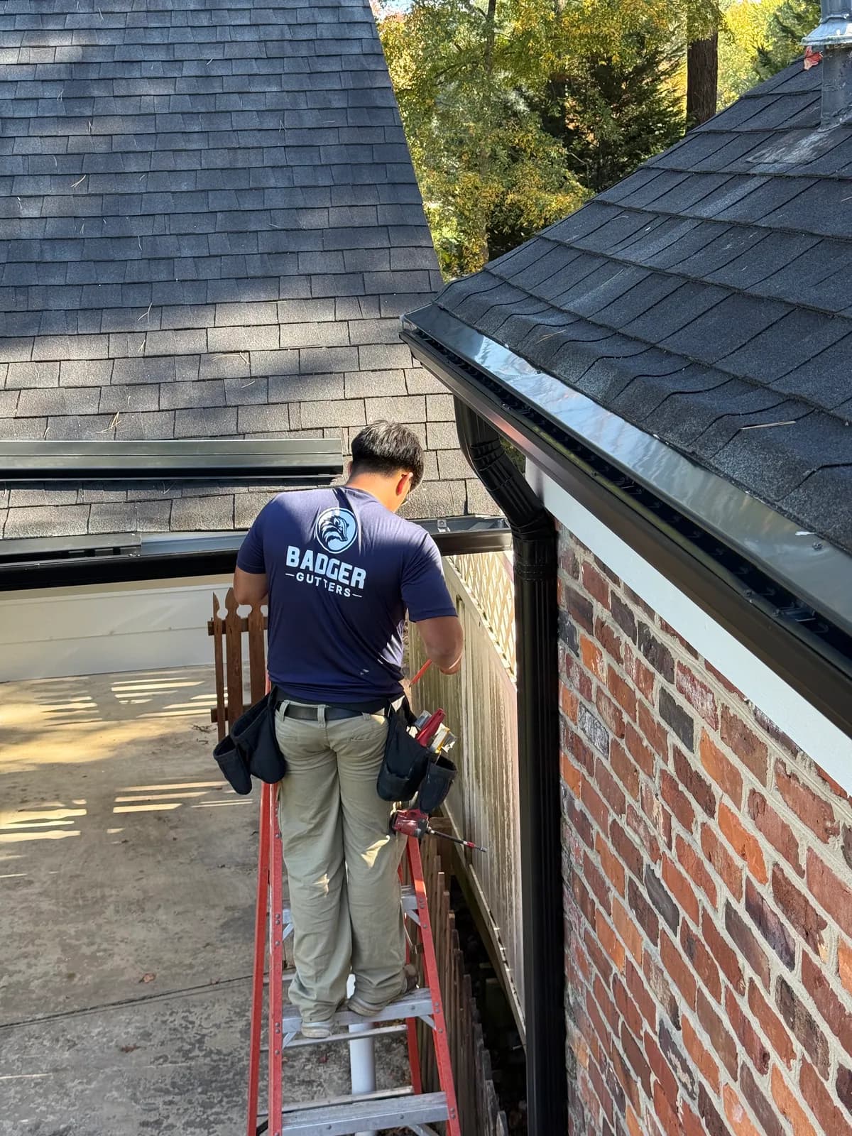 Badger Gutters installer on a ladder fitting a black gutter and downspout on a brick house in the Charlotte, NC area