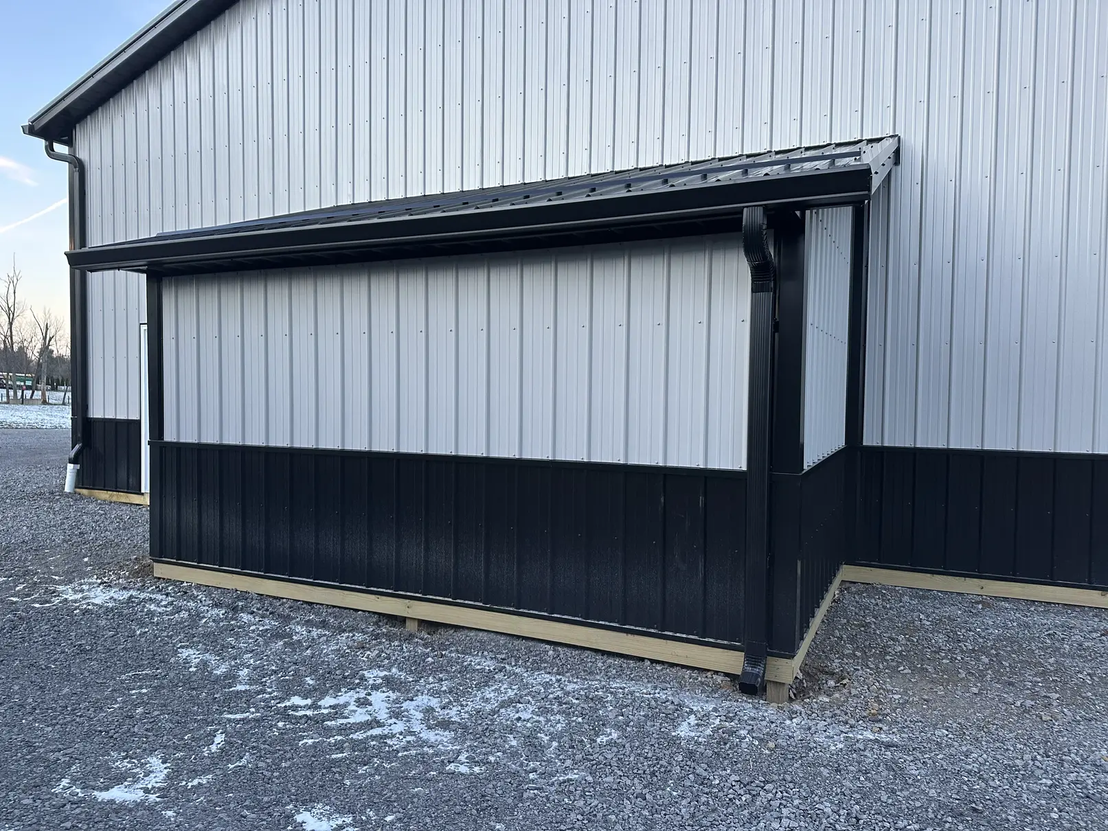 Black seamless gutter and downspouts on the lean-to of a gray and black metal building