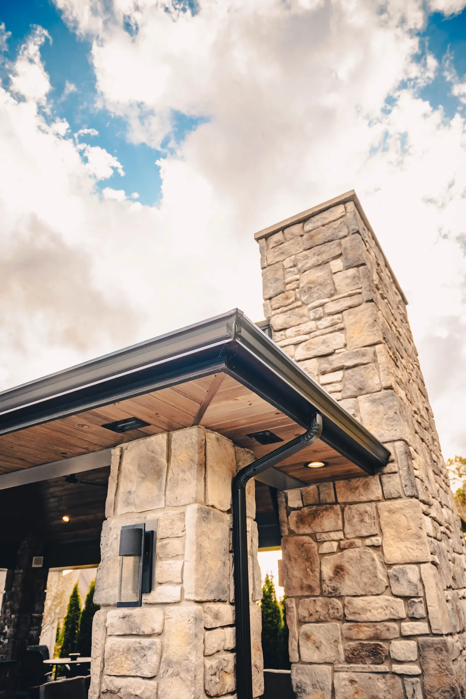 Black seamless gutter with a strip miter corner and downspout on a stone outdoor pavilion