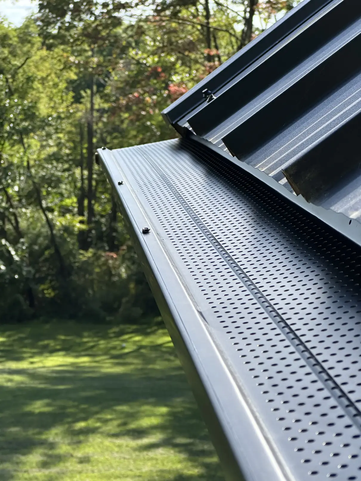 Black perforated aluminum gutter guard installed on a standing seam metal roof