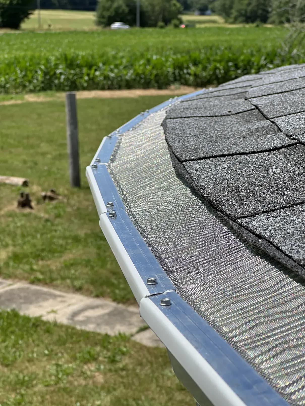 Stainless steel micro-mesh gutter guard installed on a white gutter along a shingle roof edge