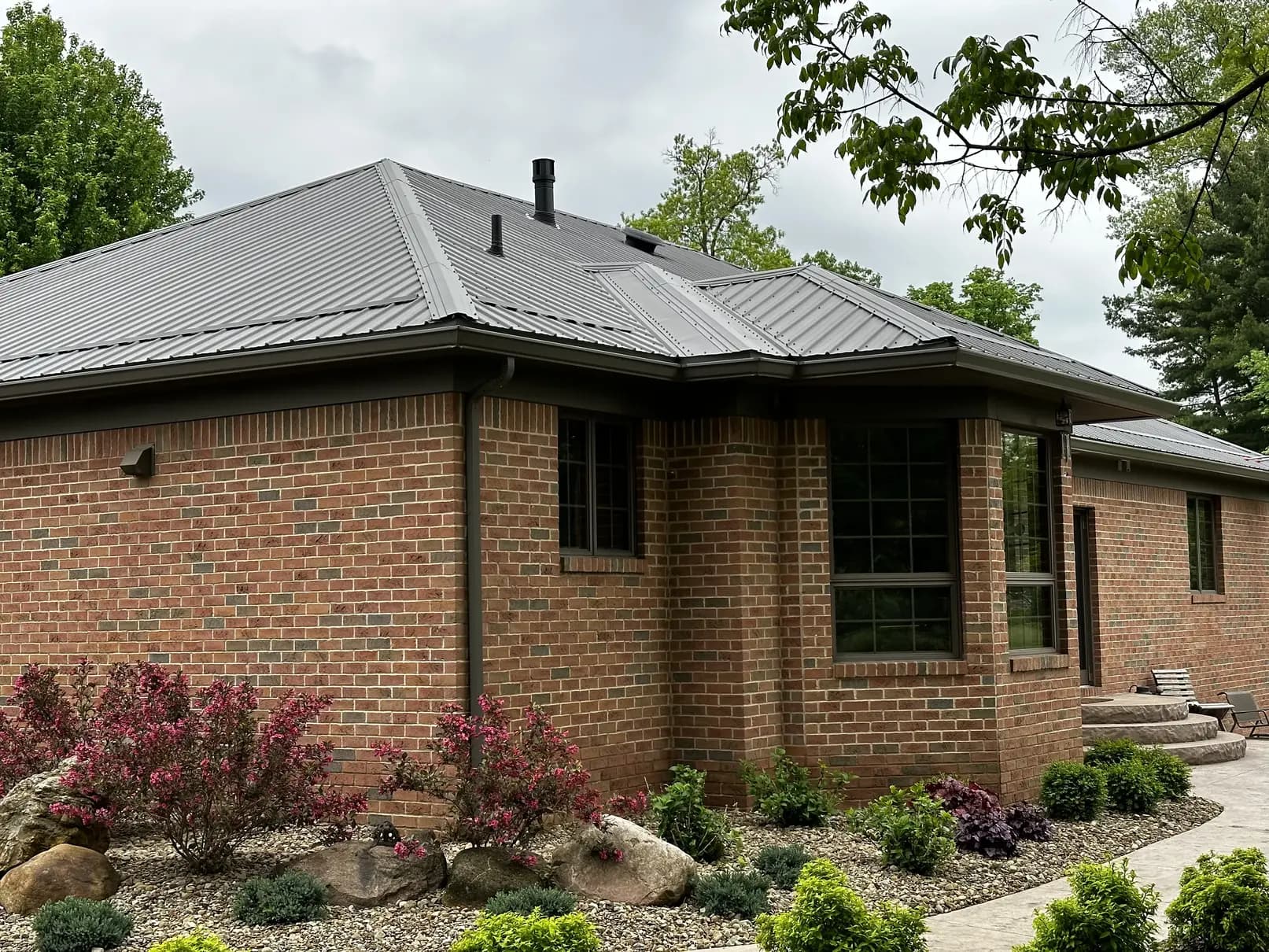 Brick home with a standing seam metal roof and new dark bronze seamless gutters and downspouts