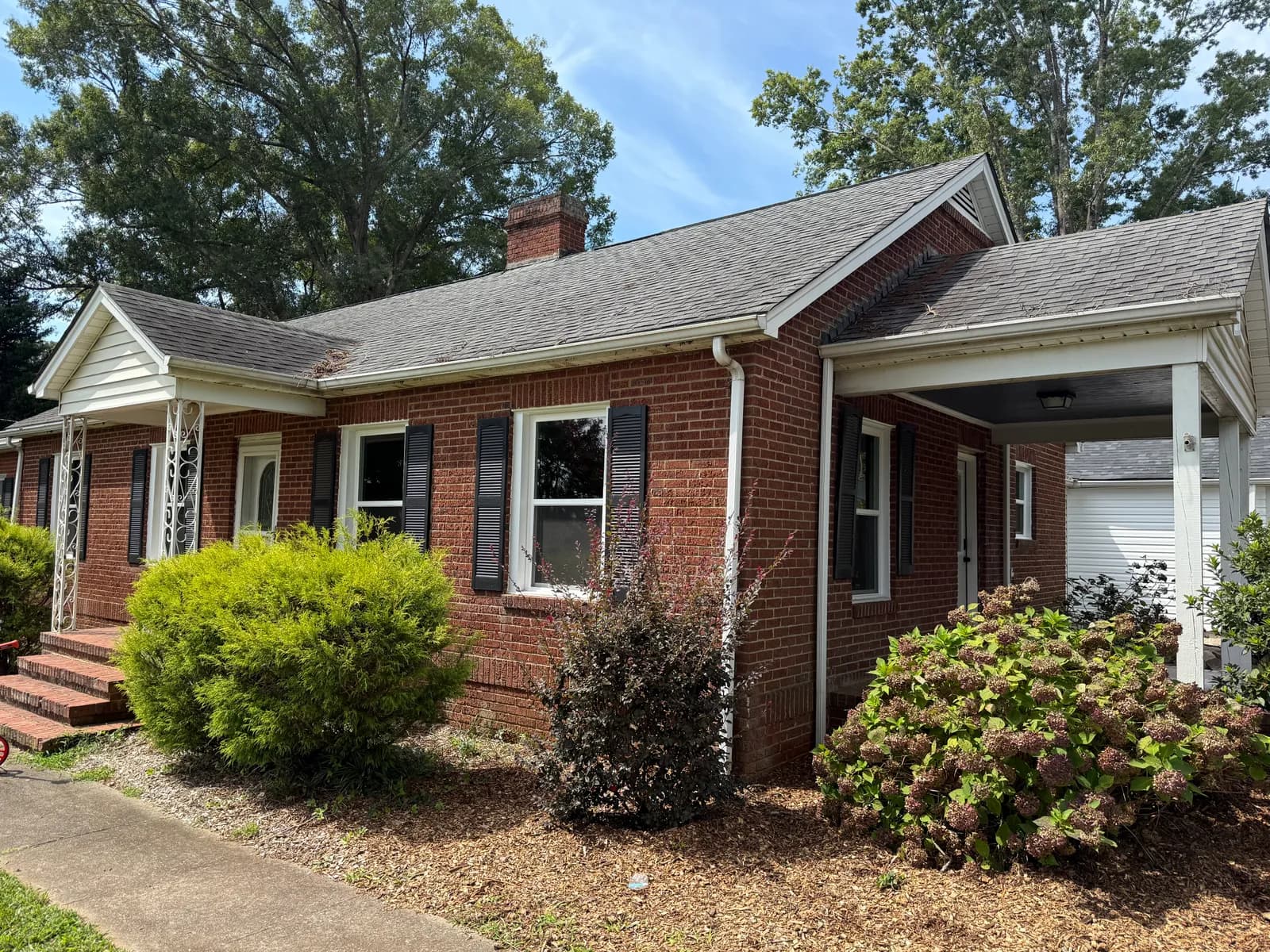 1950s brick ranch with white gutters and downspouts, black shutters and a side carport in the Charlotte, NC area