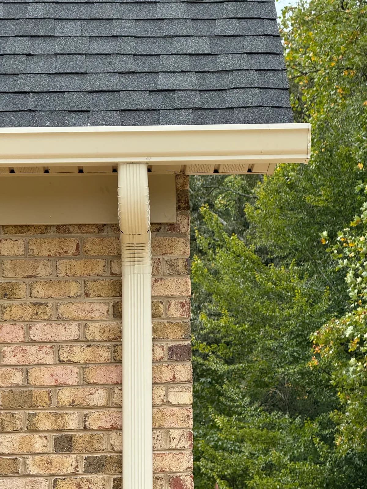 Almond gutter and downspout on a tan brick home with dark shingles in the Charlotte, NC area