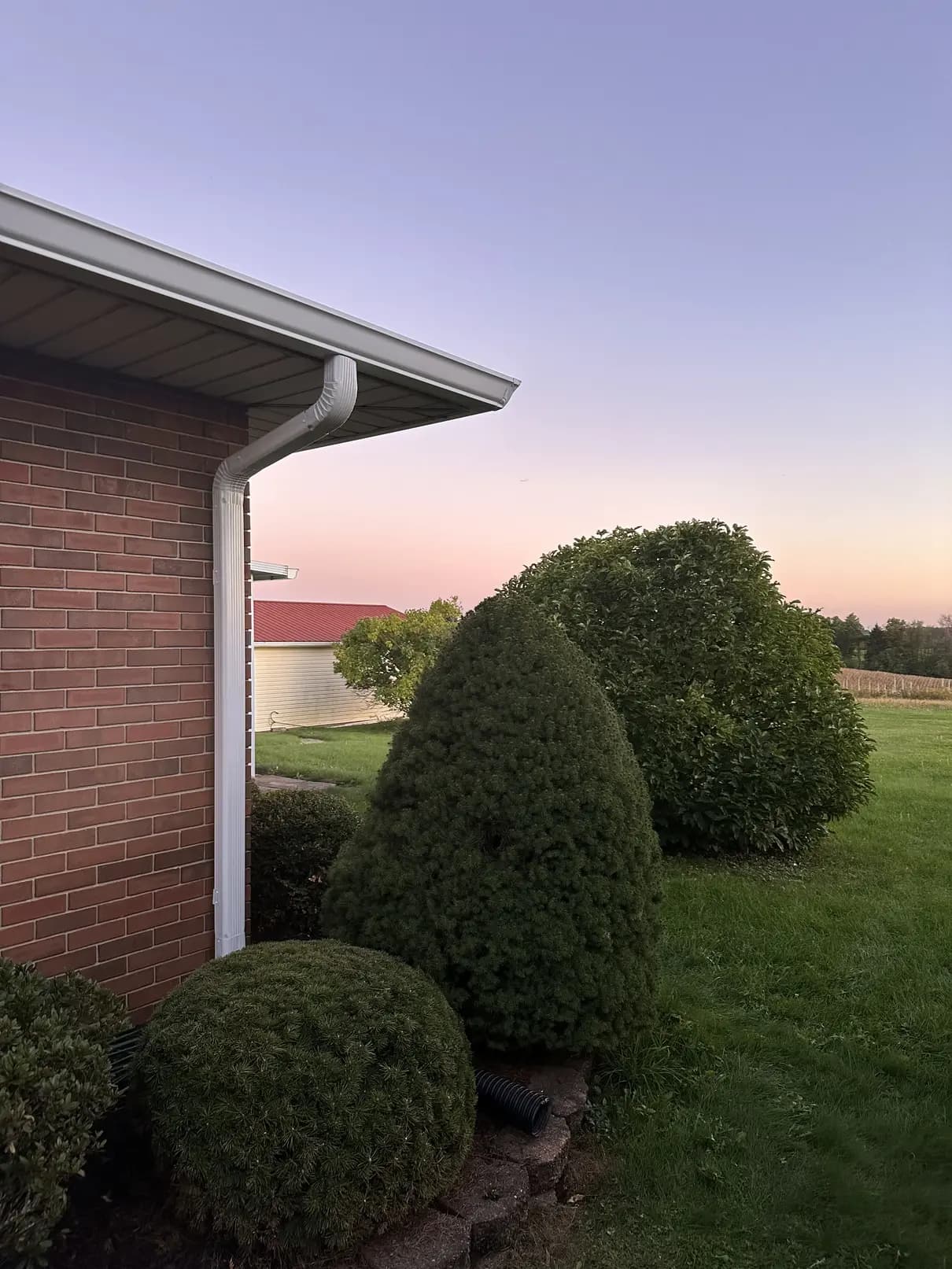 White seamless gutter and downspout on a brick ranch home at dusk